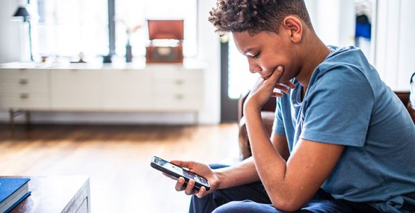 A boy sits in a waiting room, looking at his phone.  